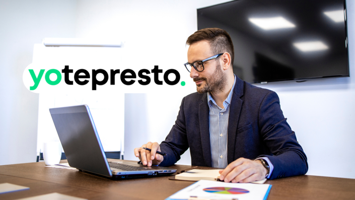 Hombre con traje y gafas trabajando en su escritorio de oficina usando una computadora portátil
