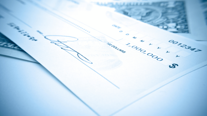 Un cheque firmado con un monto en dólares sobre una mesa con billetes al fondo. La imagen resalta la relevancia de los cheques y pagarés en transacciones financieras, así como la necesidad de seguridad al utilizarlos. Los detalles como la firma y el monto resaltan la importancia de revisar cuidadosamente cada documento antes de emitirlo o recibirlo.