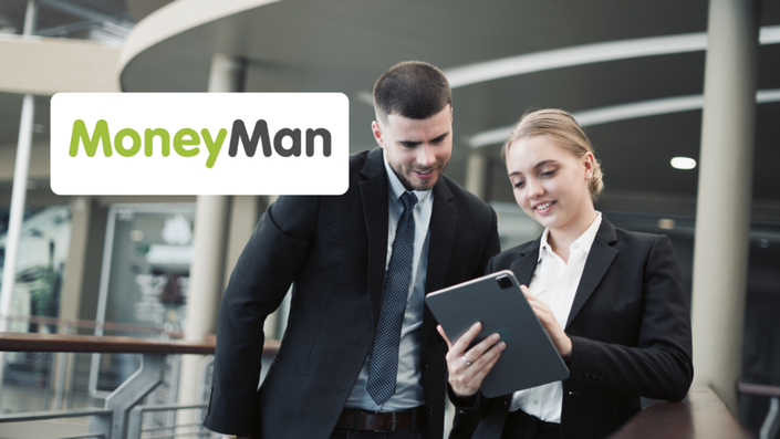 Dos profesionales de negocios, un hombre y una mujer vestidos con trajes formales, están en un entorno corporativo moderno. La mujer sostiene una tableta mientras ambos sonríen y la observan. En la imagen, aparece el logotipo de MoneyMan, una empresa de préstamos en línea.