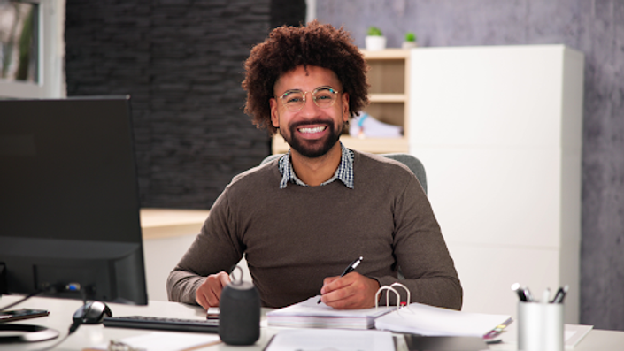 hombre sonriendo en su escritorio mientras toma notas frente a su computadora con el beneficios de abrir una cuenta digital