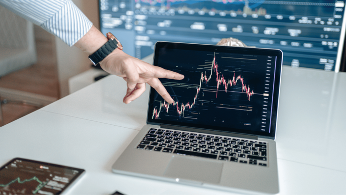 Persona señalando un gráfico de inversiones en su computadora portátil, ilustrando el proceso de Invertir en la Bolsa Mexicana.