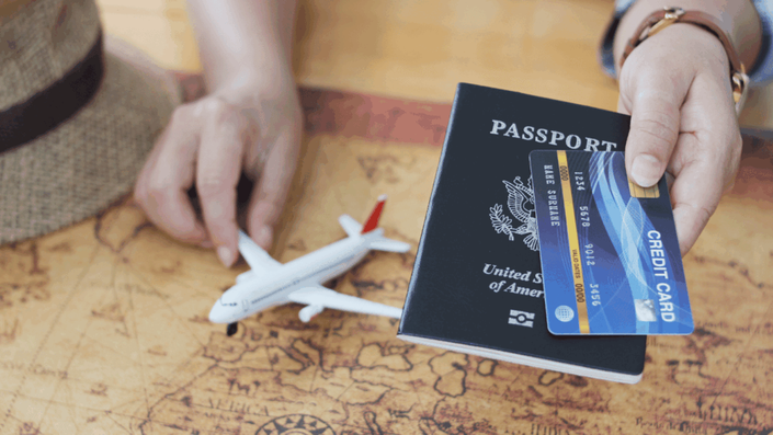 Una persona sosteniendo un pasaporte y una tarjeta de crédito sobre un mapamundi con un avión de juguete al lado, planificando un viaje usando Tarjetas con recompensas para acumular millas.