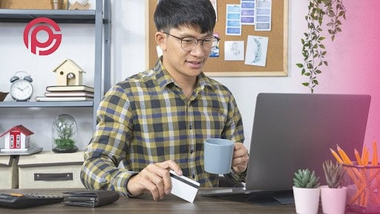 el hombre mira felizmente la pantalla del portátil sosteniendo una taza y una tarjeta de crédito