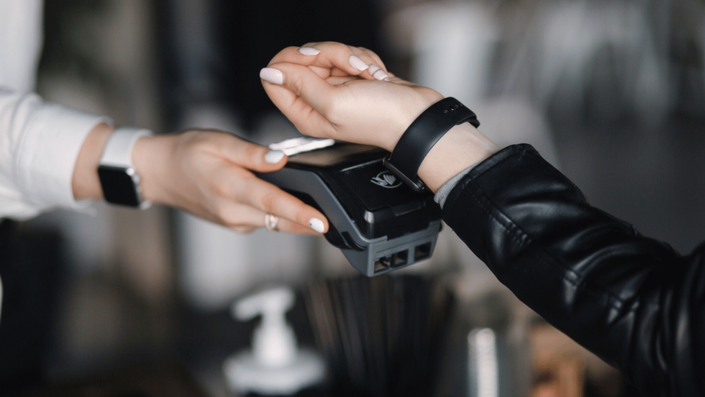Persona realizando un pago sin contacto con billeteras digitales a través de un smartwatch en un terminal de pago.